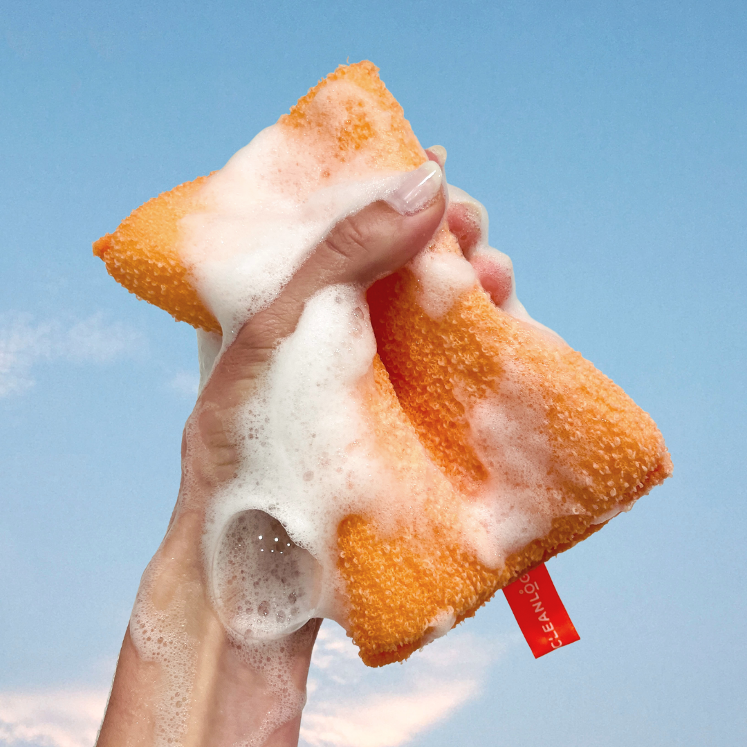 Hand holding a foamy orange cleaning cloth against a blue sky background