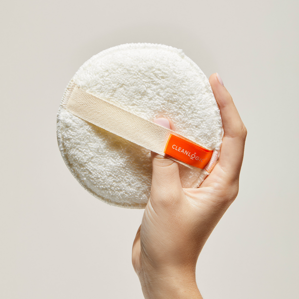Hand holding a white round cleaning pad with a visible brand label against a neutral background