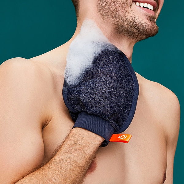 Man using a blue exfoliating glove on his shoulder against a teal background
