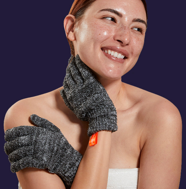 Woman wearing gray gloves with an orange label, smiling against a dark background