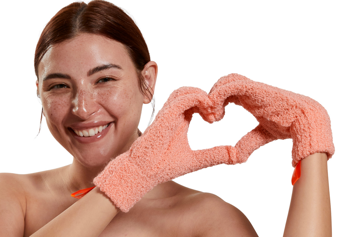 Woman wearing a pink scrubbing glove making a heart shape with her fingers on a white background