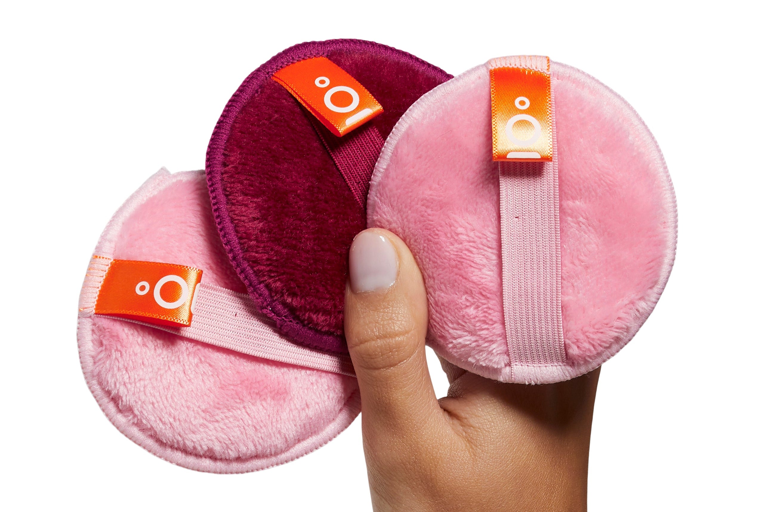 Hand holding pink and purple makeup removal pads with orange accents on a white background