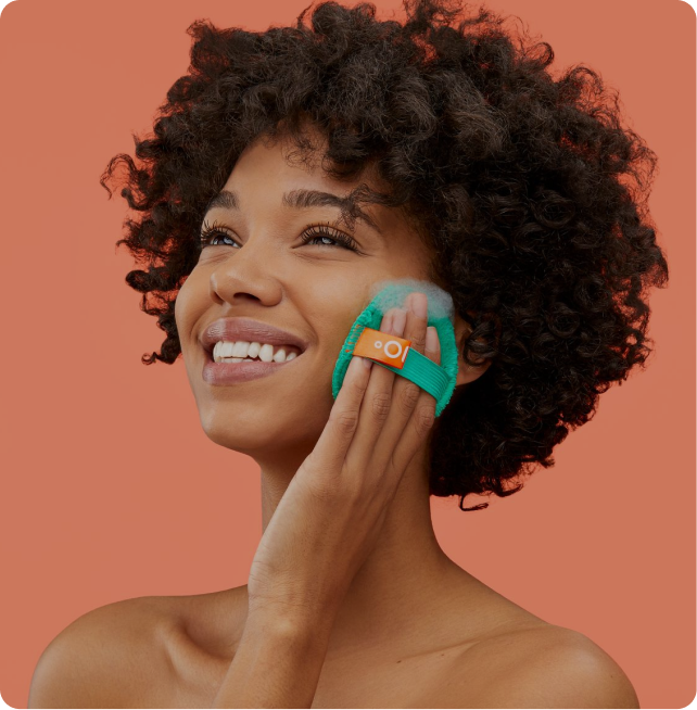 Woman applying a green facial cleansing pad to her face against a peach background