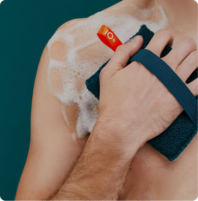 Hand using a blue scrubber on a shoulder with soap suds, against a teal background.